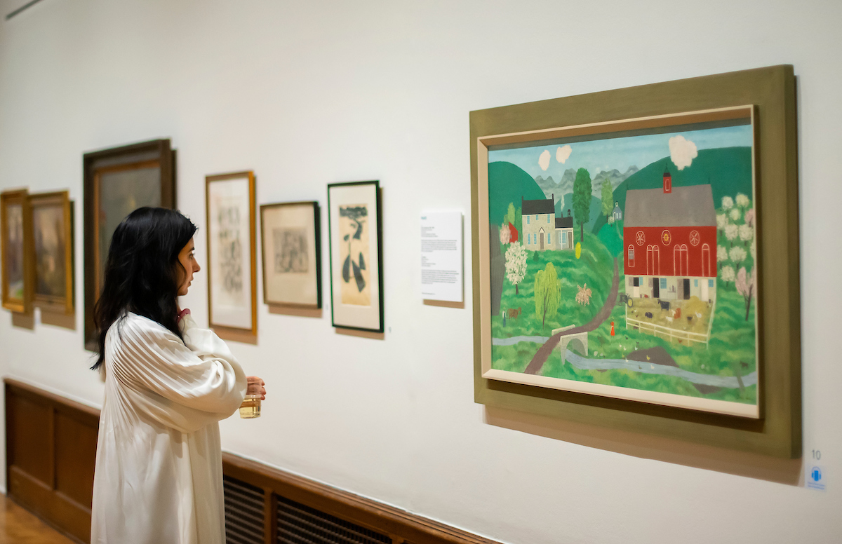 woman in profile looking at folk art painting of a red barn and white farmhouse