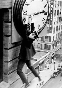 Actor Harold Lloyd hanging from a huge clock face on a tall city building.