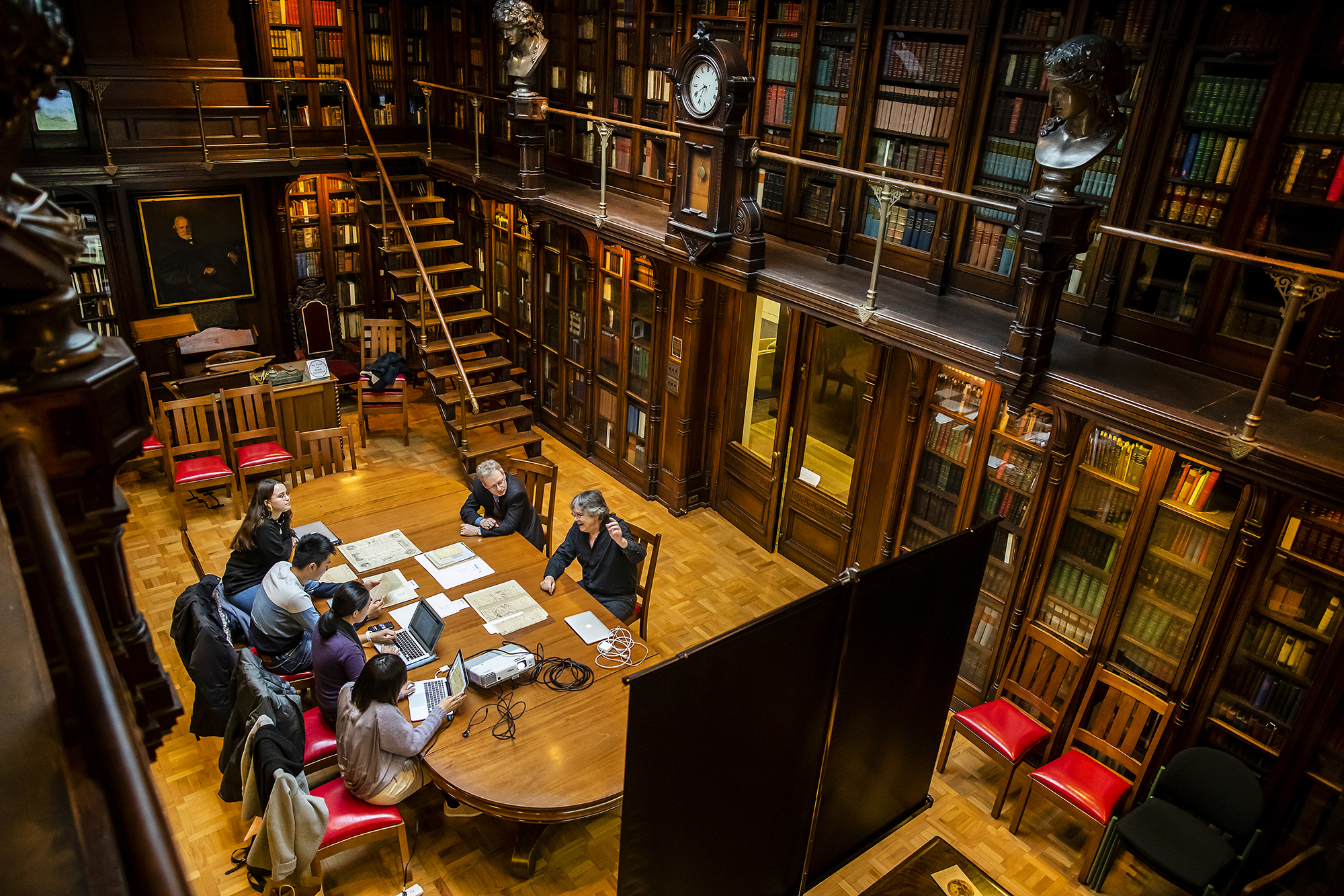 Overhead shot of students and professors around table in historic library.