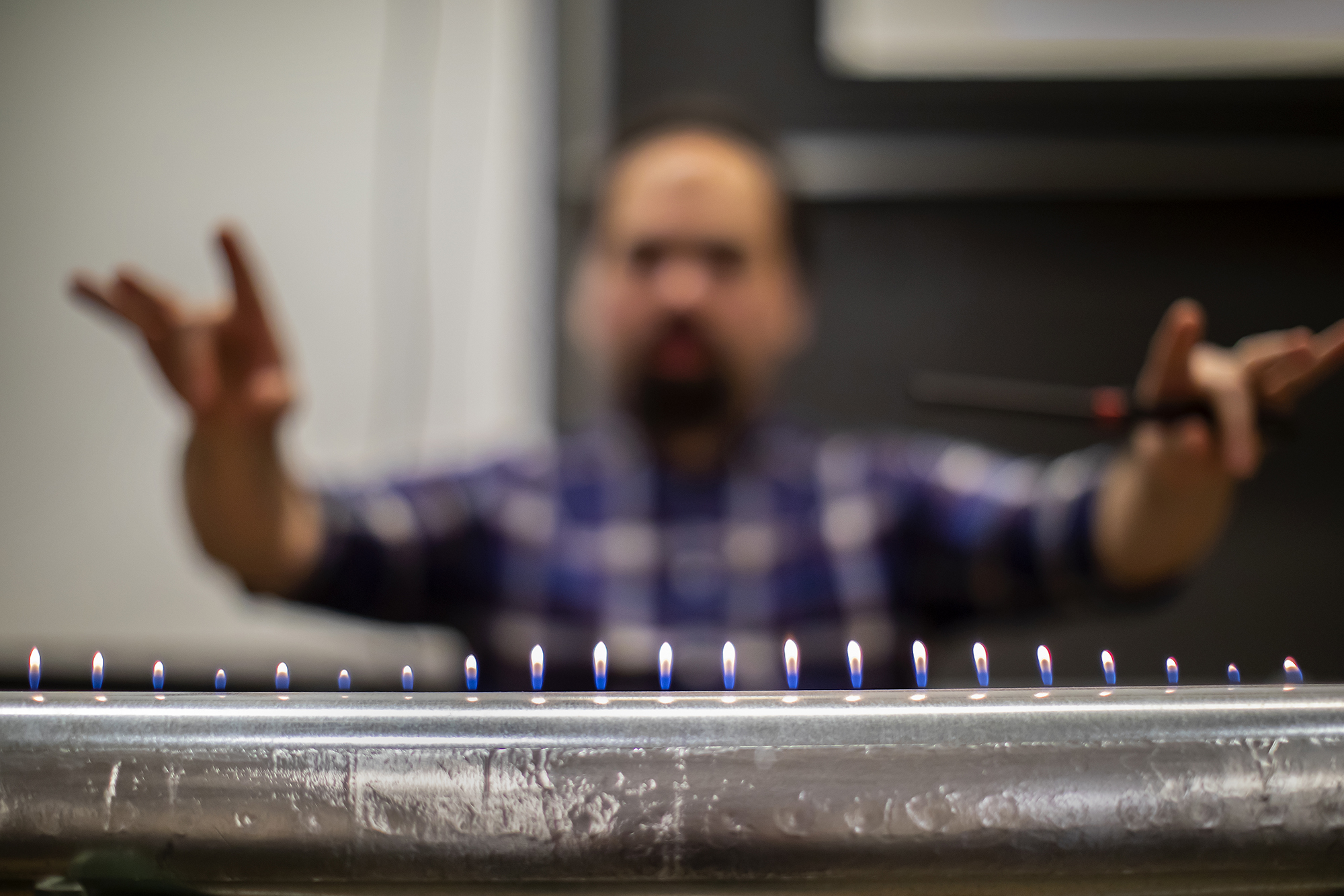 a metal tube with a line of flames coming out of the top and a blurred person posing in the background