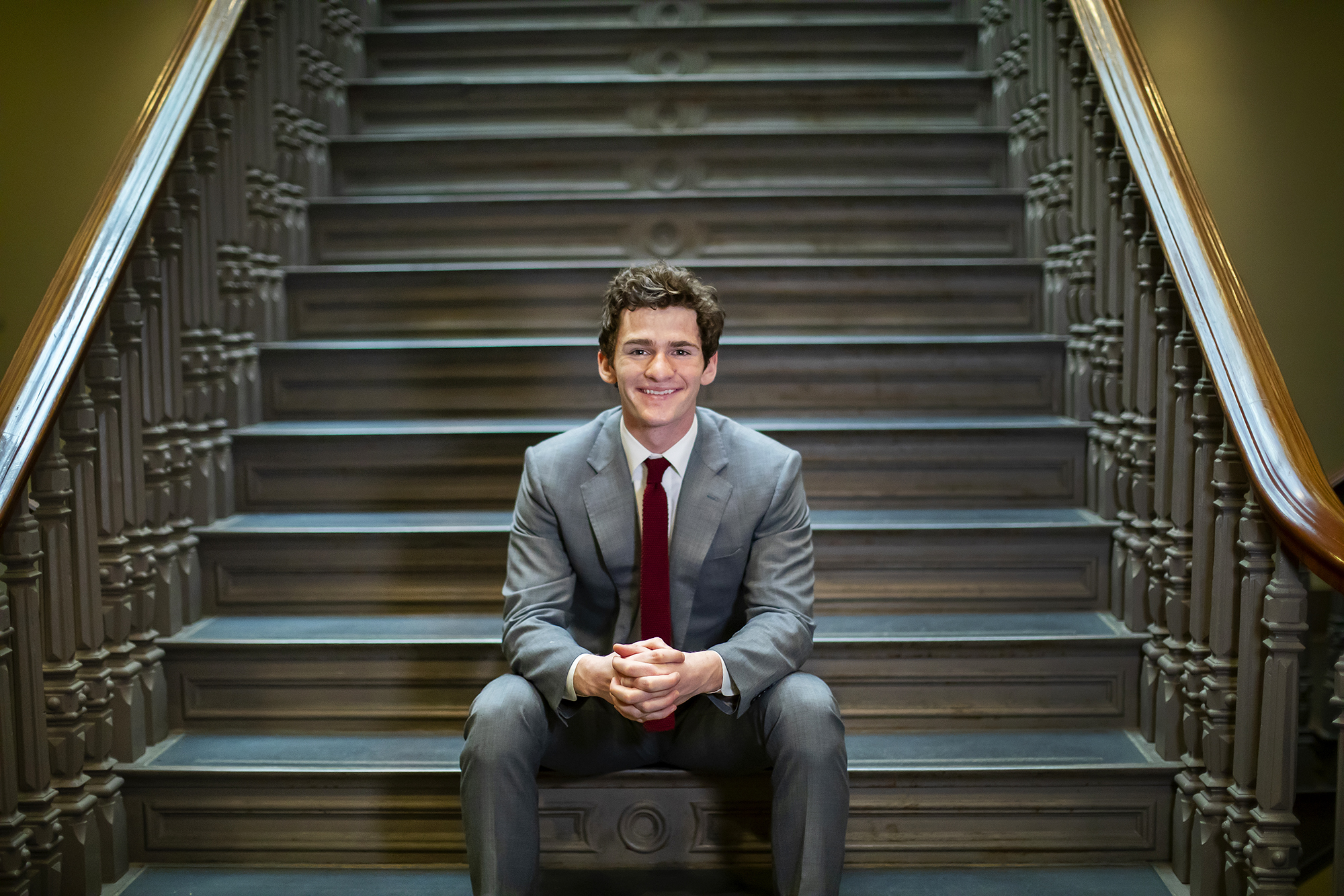 Student sitting on steps wearing a suit and tie. 