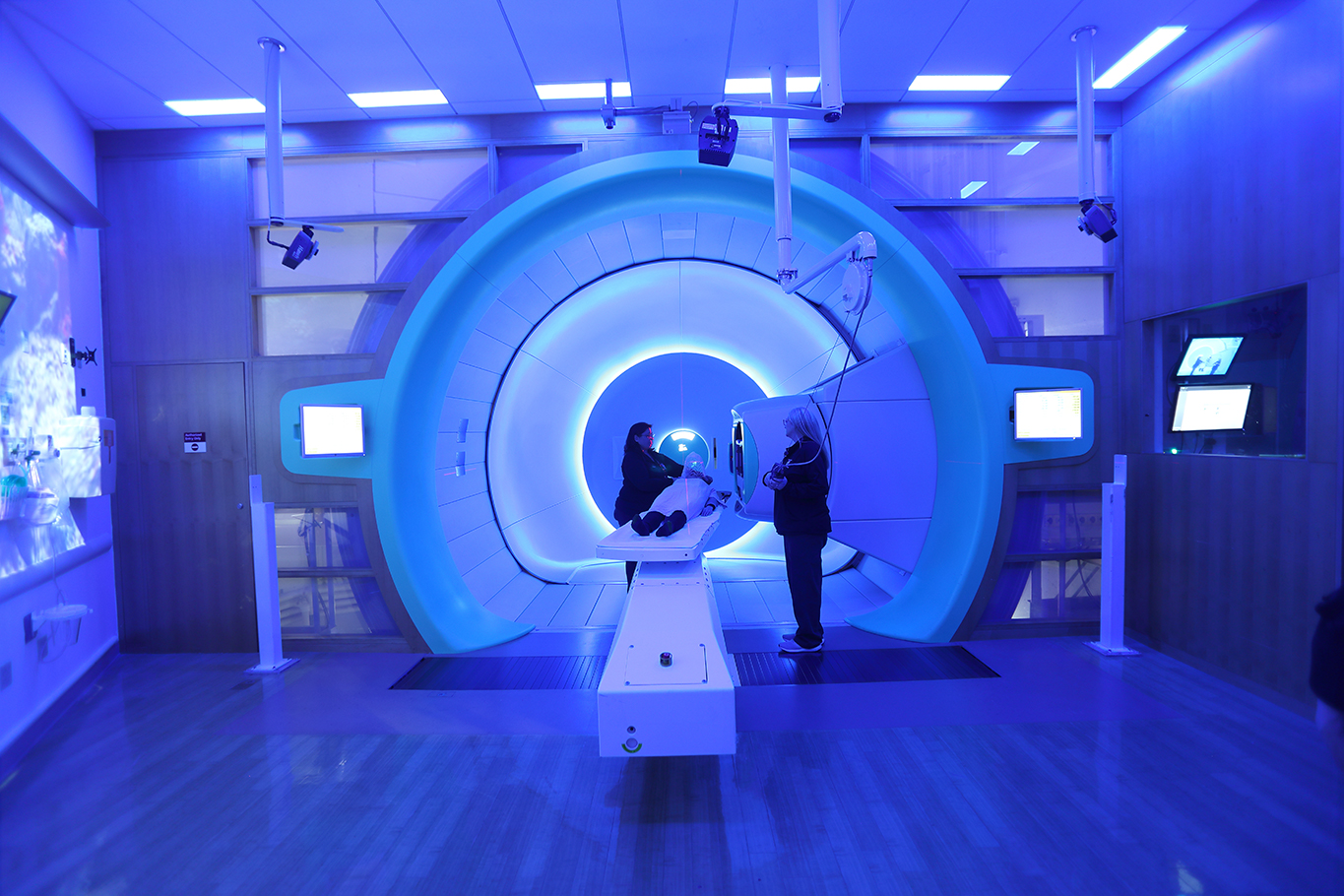 A patient is prepared to receive proton therapy in a blue-lit room with a large rotational machine
