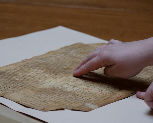 A person pointing two fingers at a very old, weathered manuscript with indistinguishable writing.