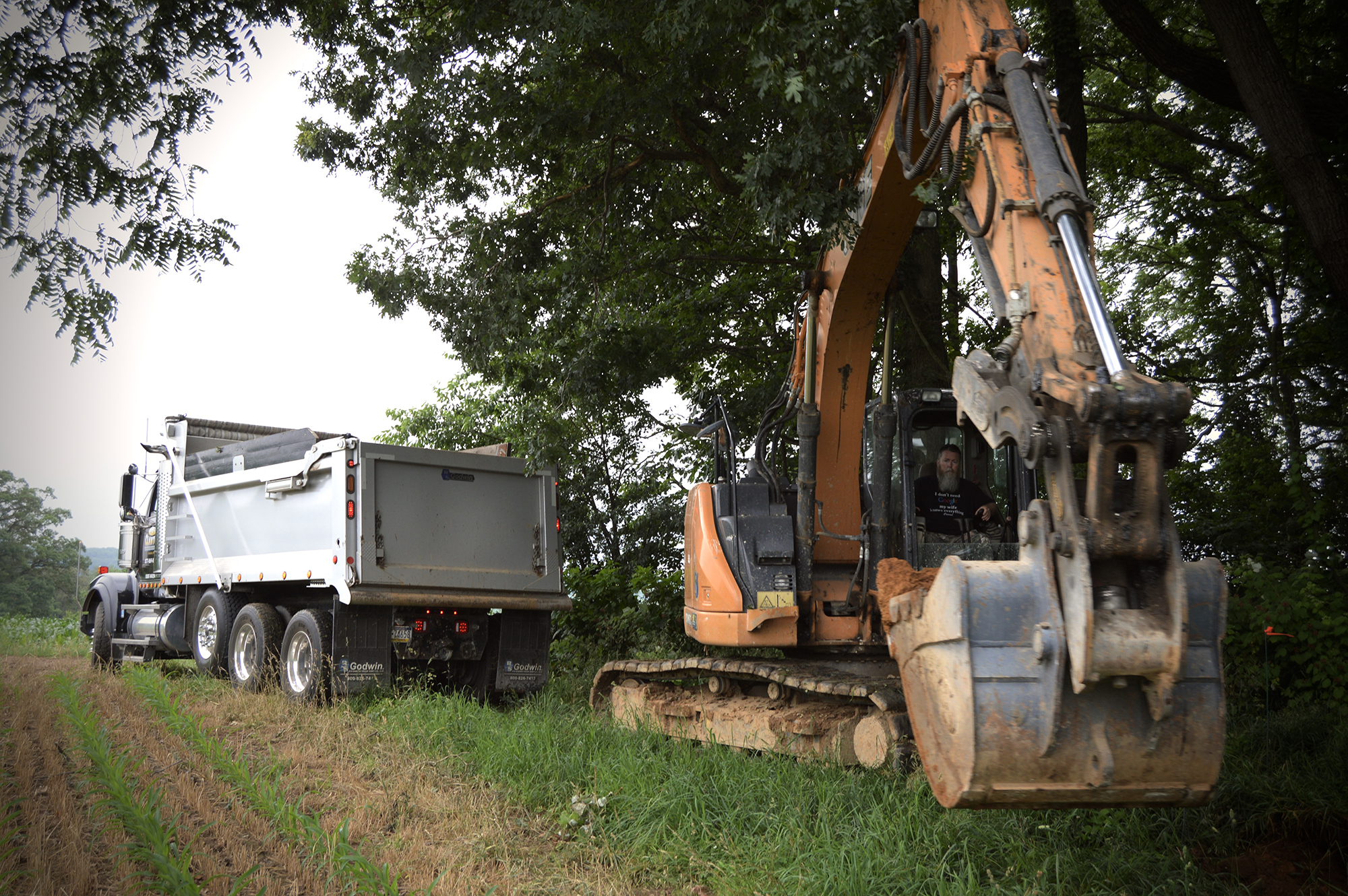 An excavator and dump truck at work on agricultural land.