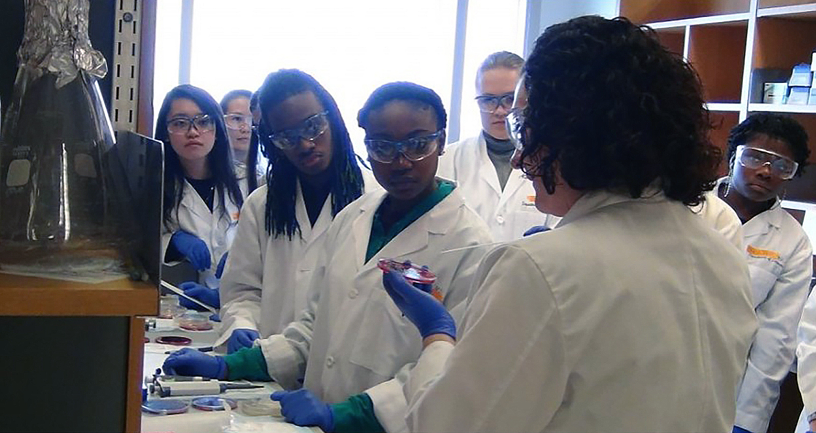 high school students in lab coats face an instructor in a reproductive science lab.