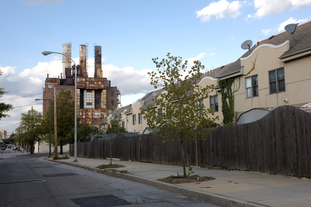 Philadelphia city street, abandoned factory in background, housing behind sidewalk fence.