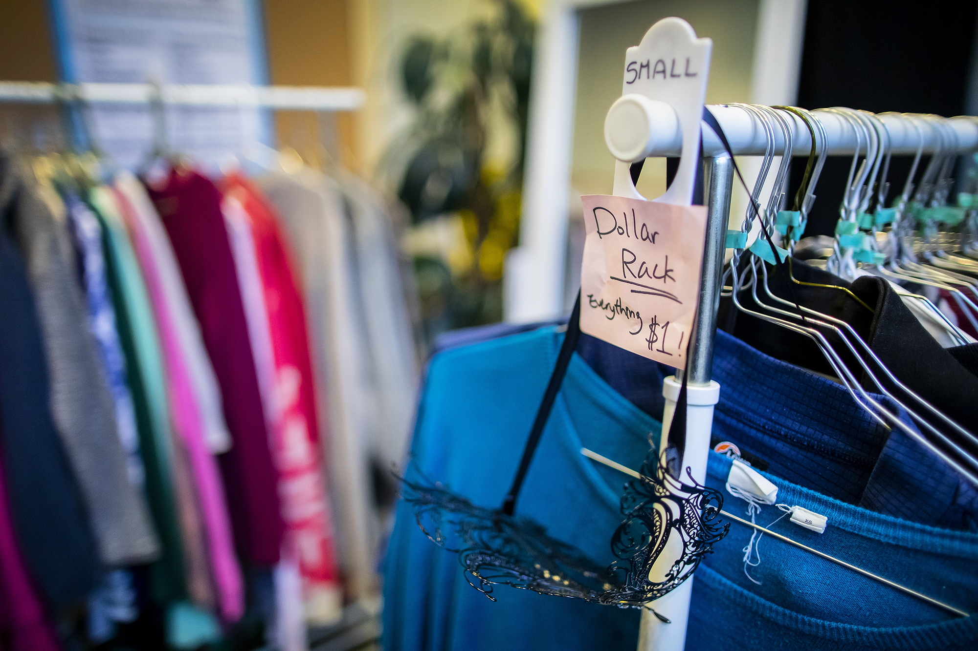 A rack of clothes in the foreground says "Dollar Rack: Everything $1!" and "Small" up top. In the background is another clothing rack, blurred out.