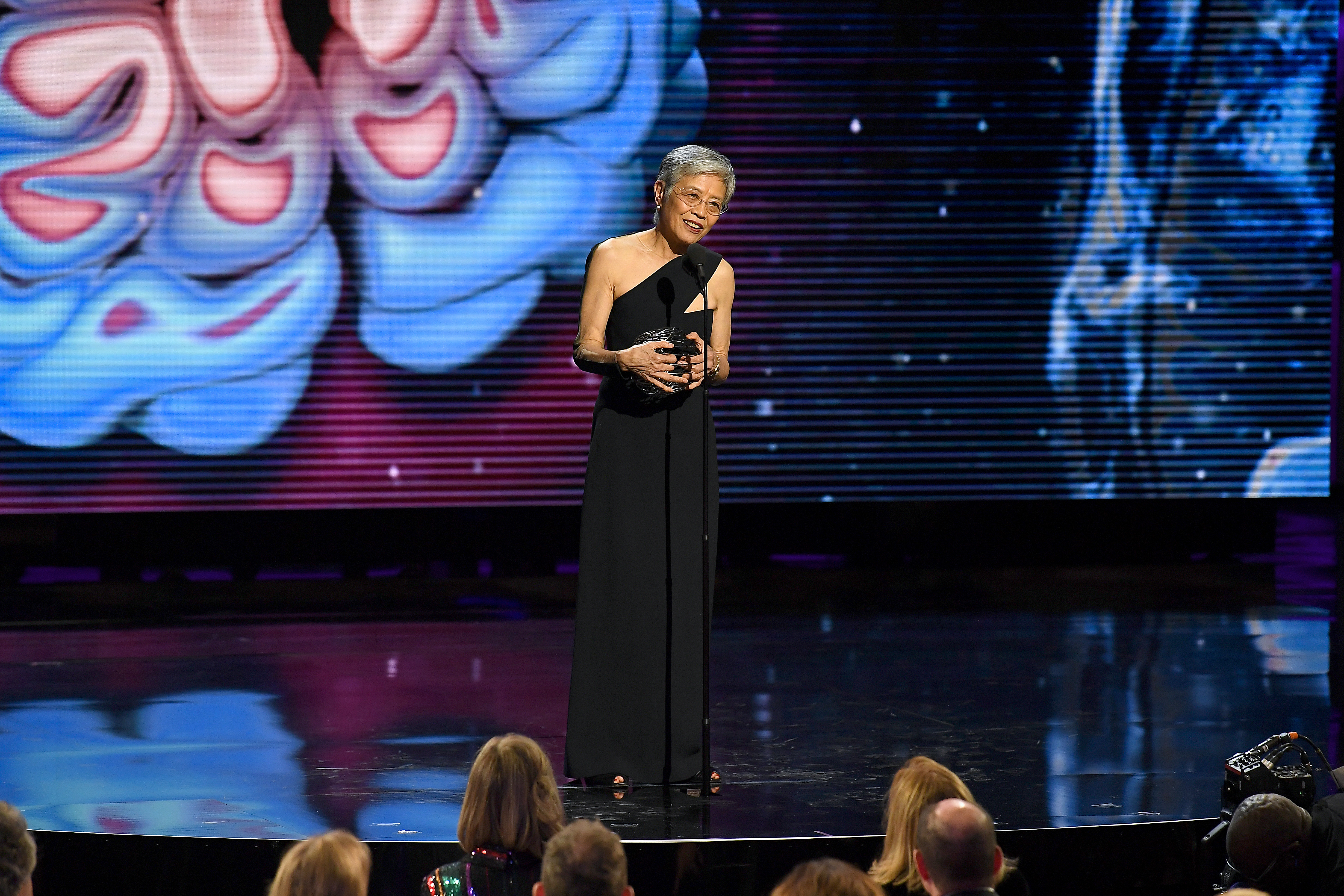 Virginia Lee stands on stage speaking into a microphone accepting her Breakthrough Prize Award