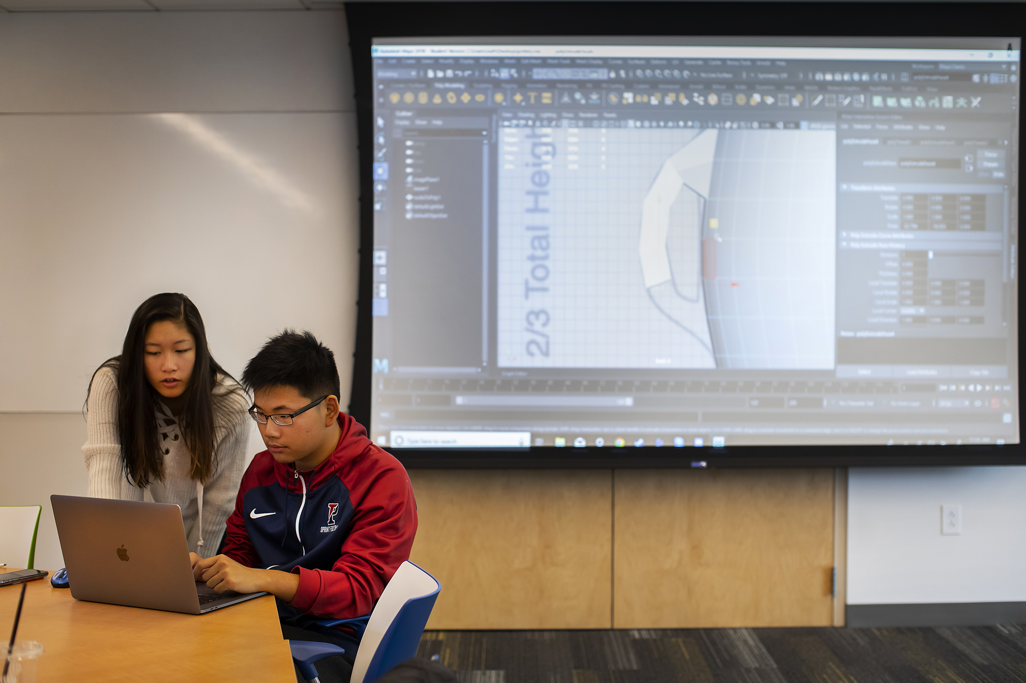 two students working on a laptop with a screen behind them