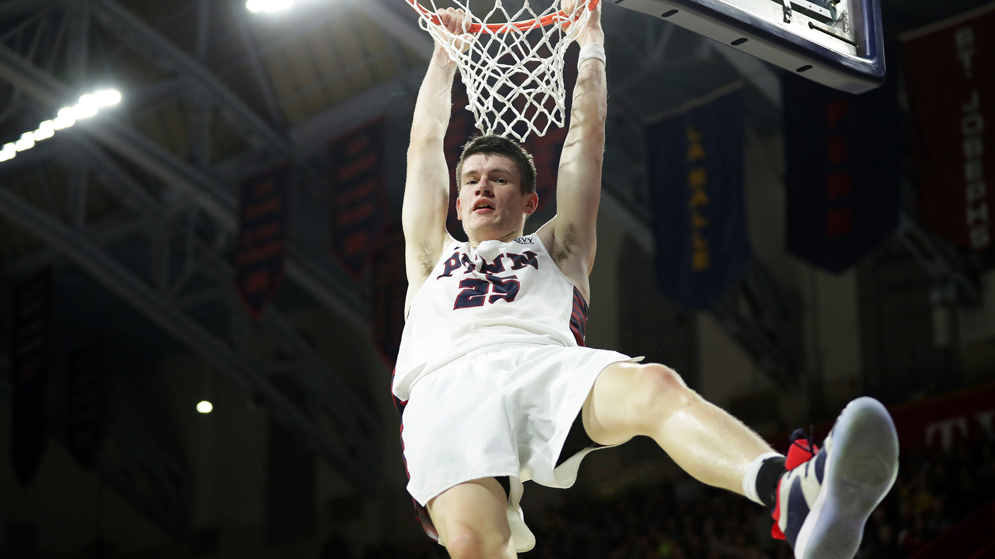 A.J. Brodeur, a junior on the basketball team, hangs on the rim after dunking at the Palestra.