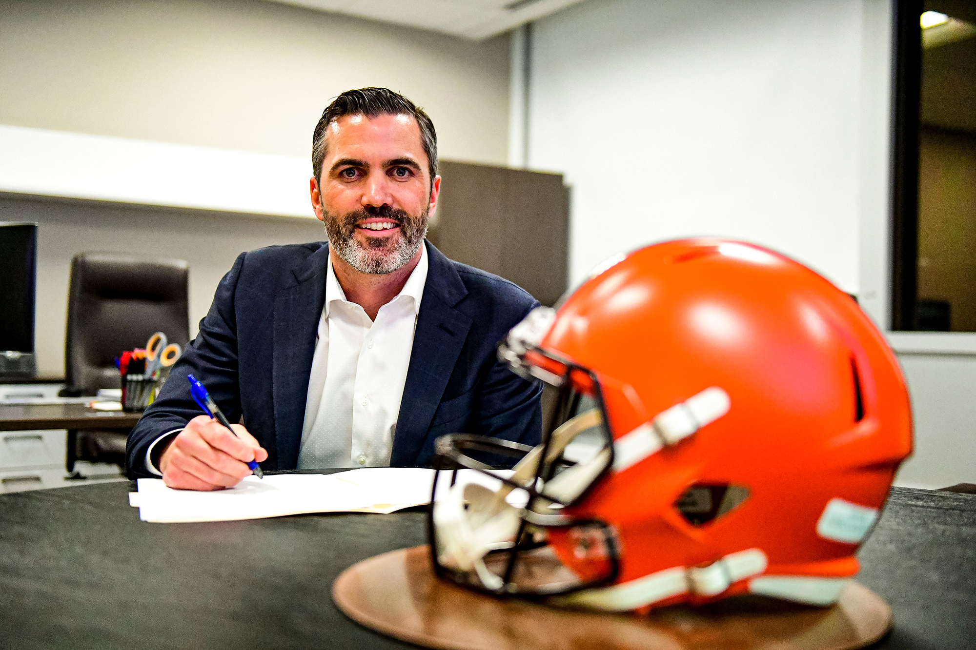 At a table containing a Cleveland Browns helmet, new Browns Coach Kevin Stefanski signs a document.