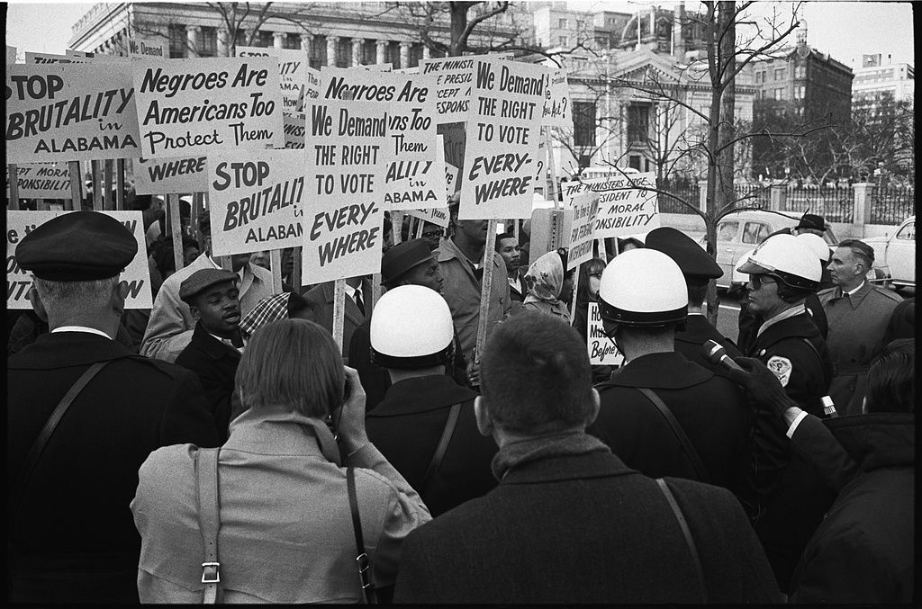 historical photo of a group of people holding protest signs  demanding the right to vote, an end to police brutality.