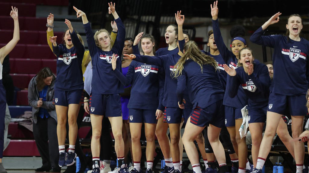 Women's basketball players on the bench hold up three fingers after a player nails a three.