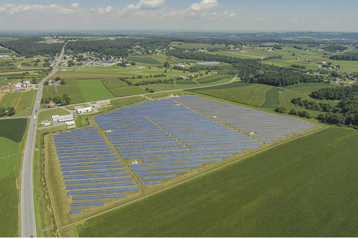 Aerial view of large greens landscape with solar panels set out over a large field. 