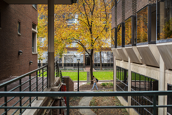 Person walking along Locust Walk seen through the bars of a railing of a campus building