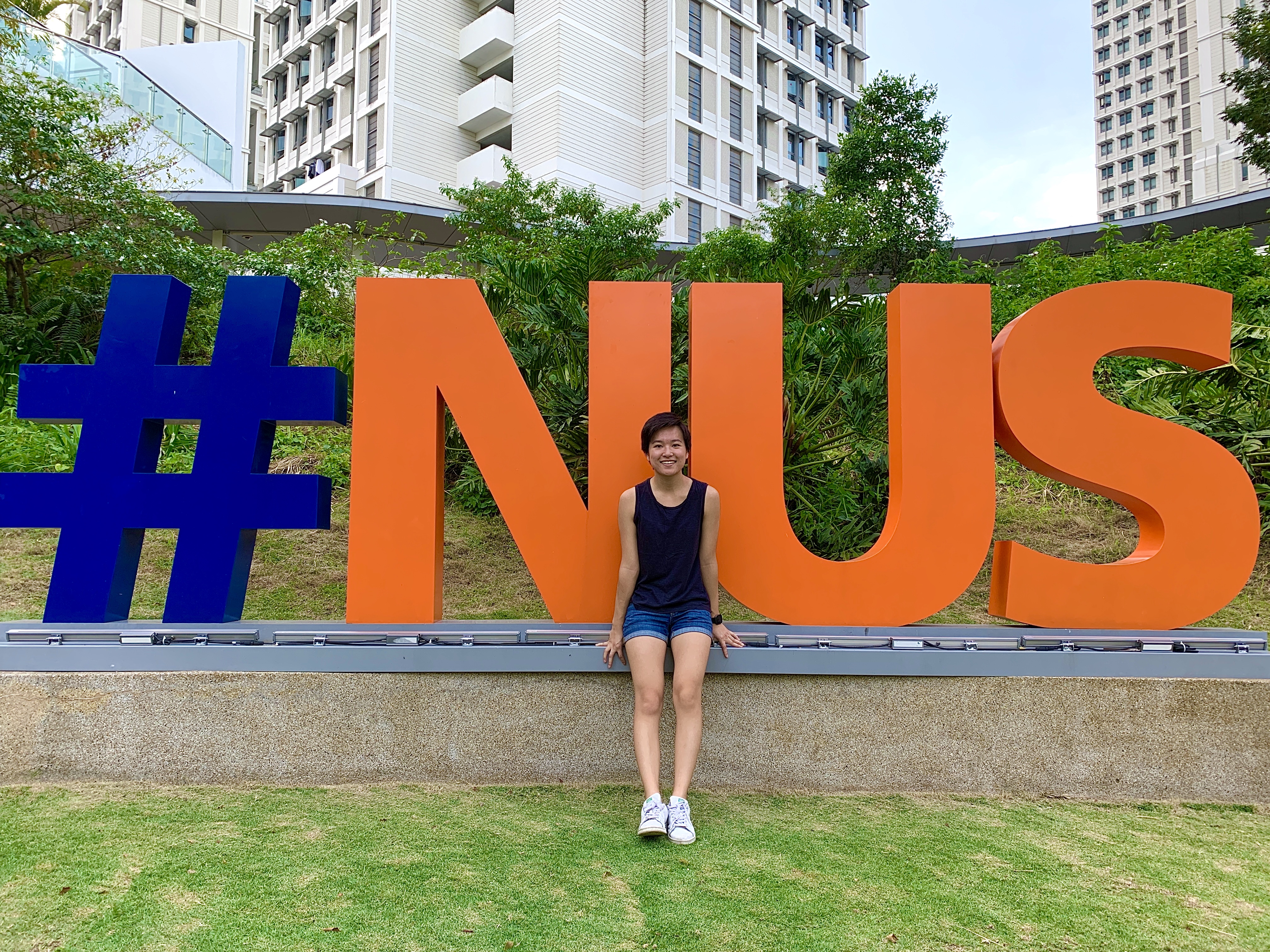 Jackie Shi sits in front of large letters on Singapore’s University campus that read #NUS