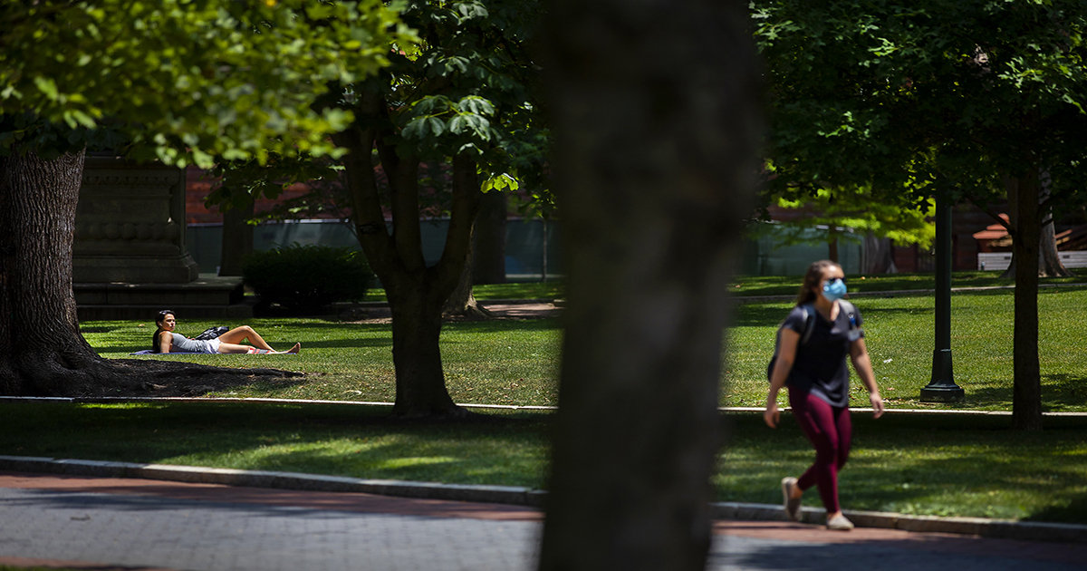 Person walking in sunshine along Locust Walk wearing a face mask.