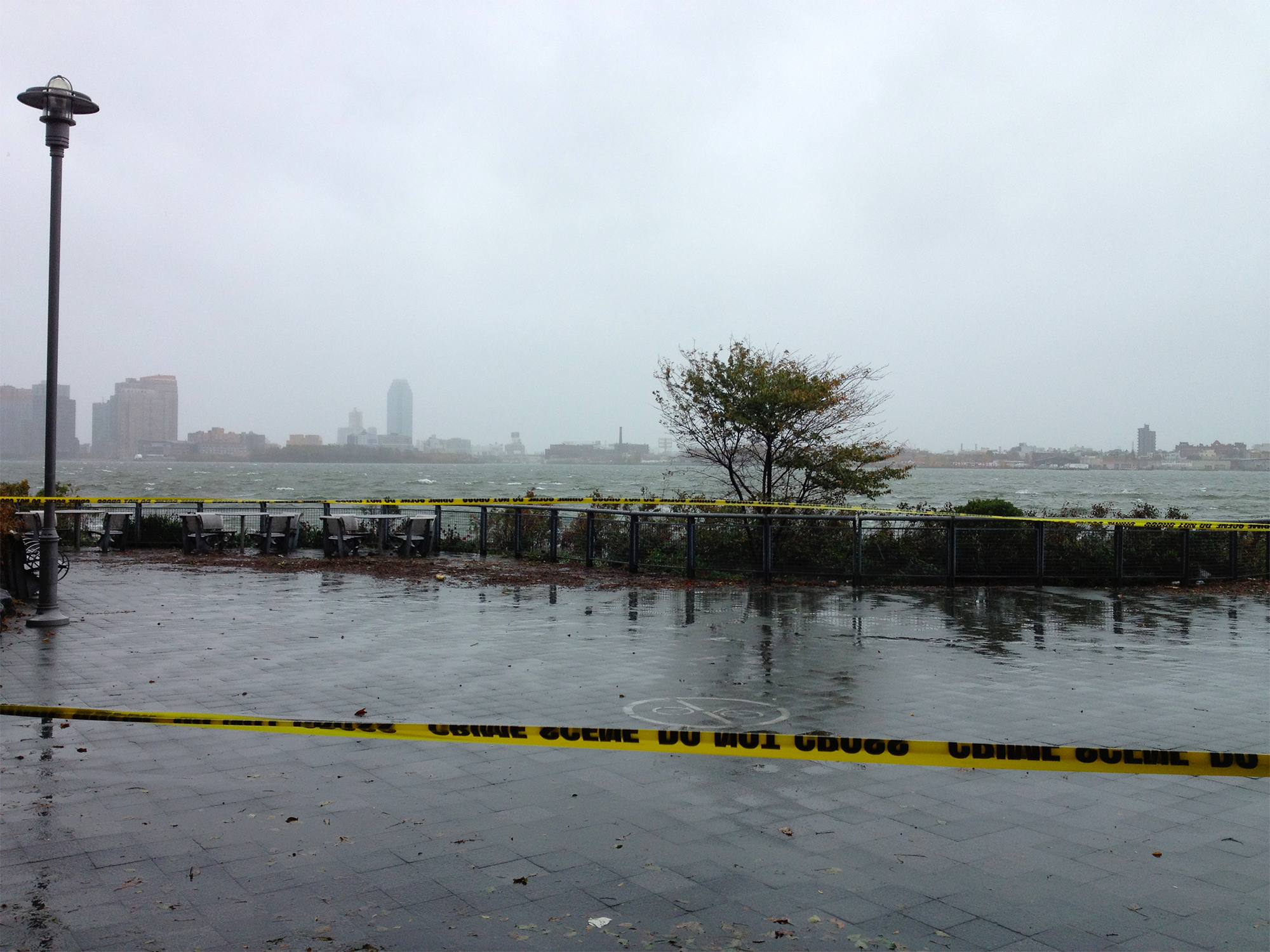A waterfront promenade taped off with police tape during Hurricane Sandy that looks out onto Brooklyn on the far shore.