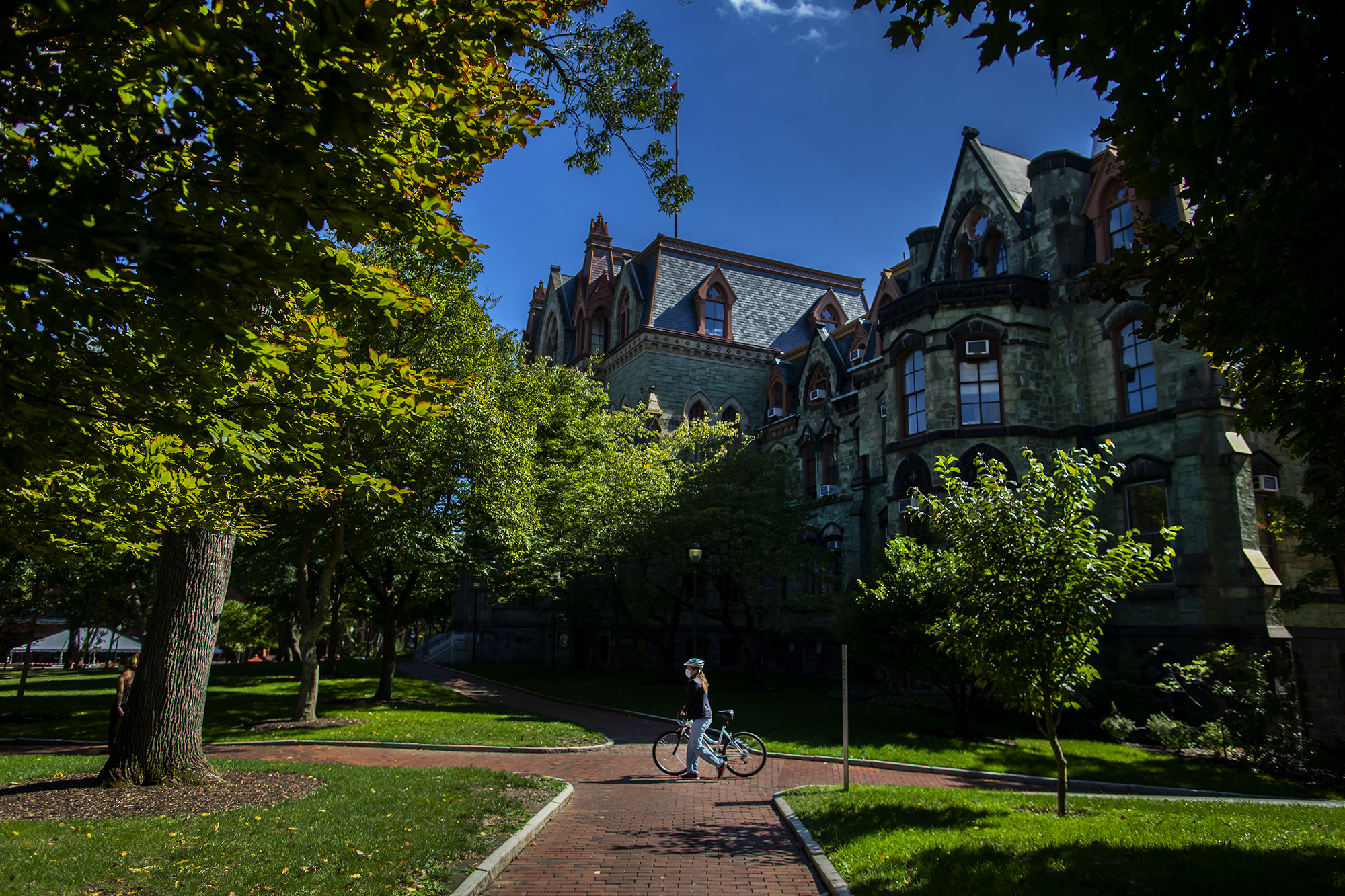 a person with a bike walking in front of college hall on a sunny day