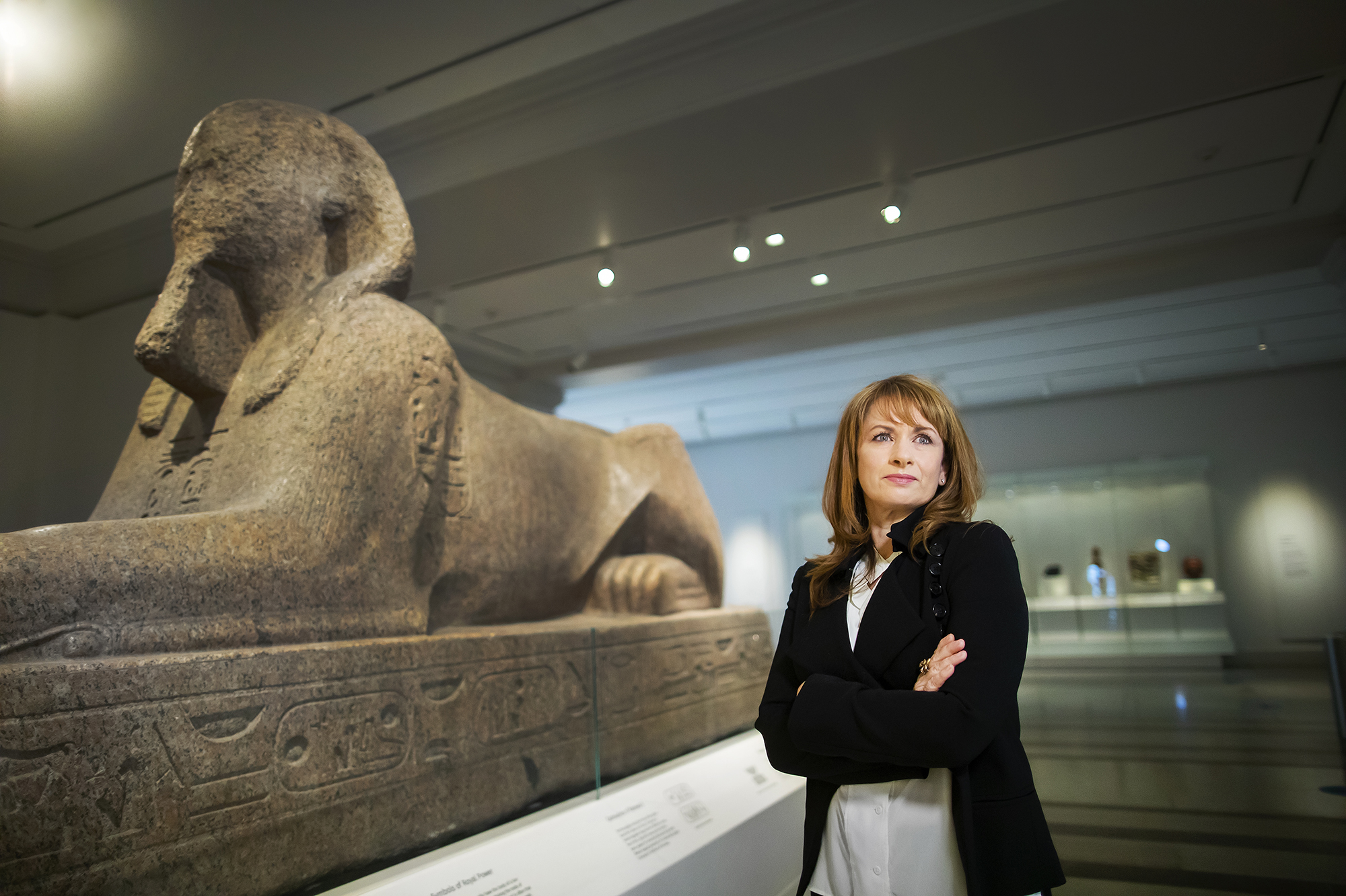 Lynn Meskell standing in the Penn Museum next to the sphinx looking ahead with arms crossed.