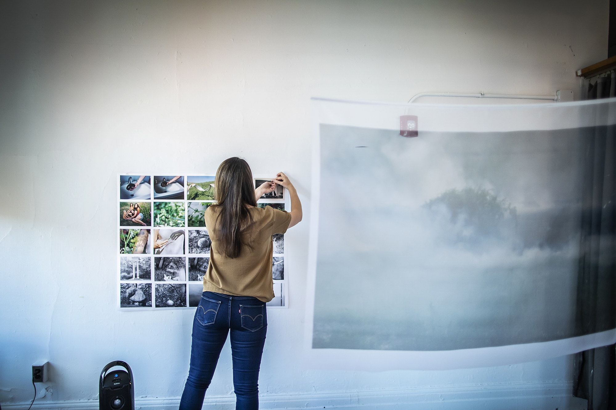 Amrita Stützle in her studio with back turned to camera pins a grid of images to her wall. 