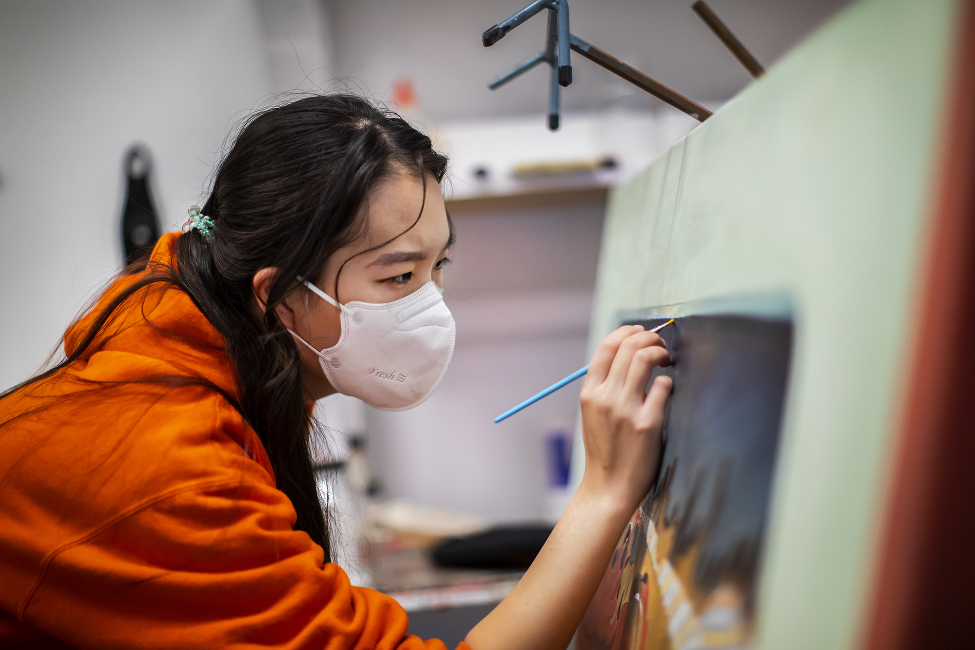 Kay (Seohyung) Lee, wearing a face mask, paints on a canvas in her studio.