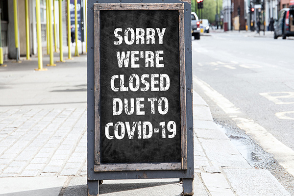 Sandwich board on a city sidewalk that reads SORRY WE’RE CLOSED DUE TO COVID-19.