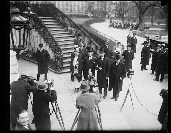 FDR arrives for his 1933 inauguration in a top hat, next to his wife Eleanor as media photographers in fedoras snap photos near the Capitol.