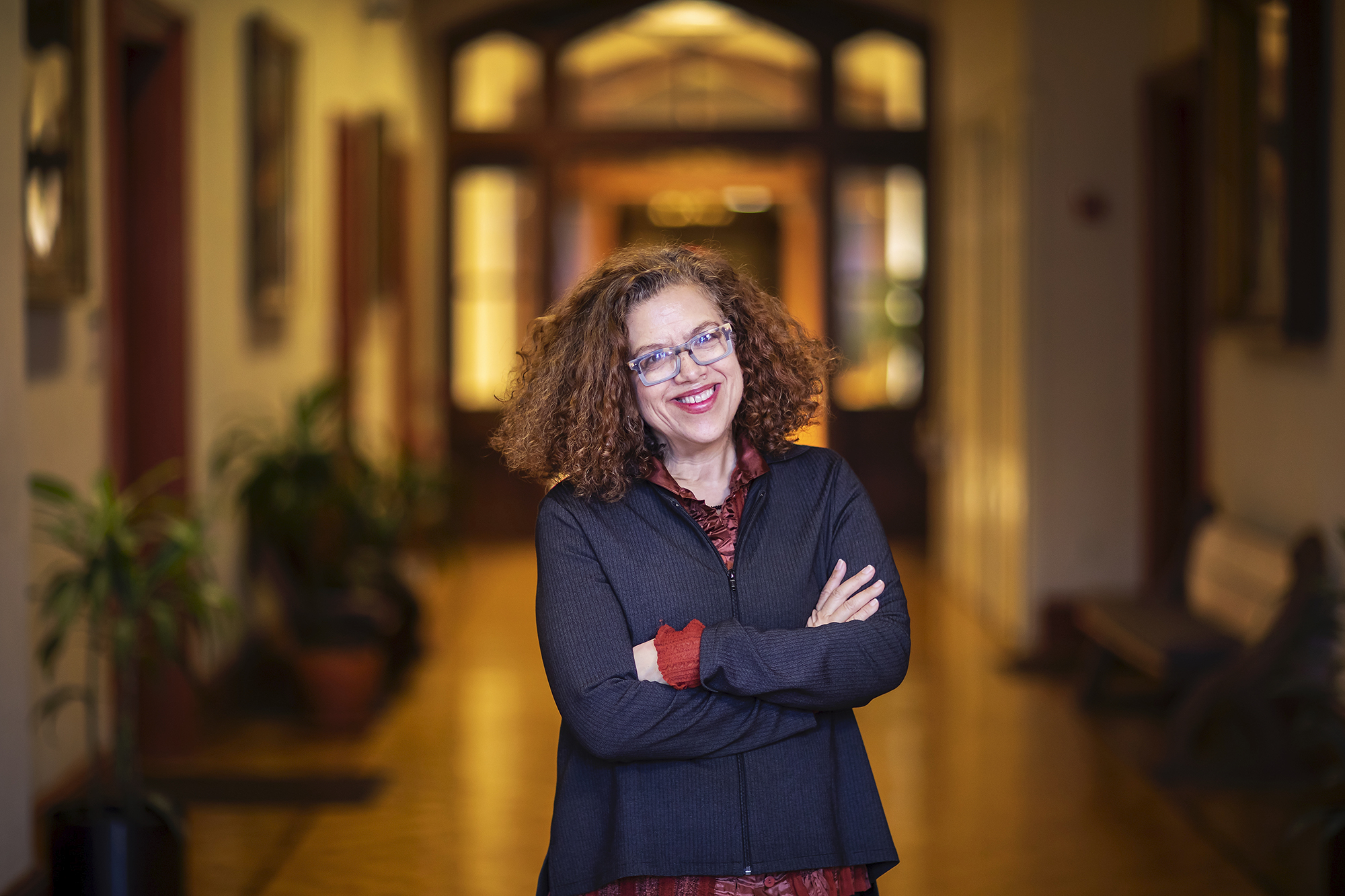 Woman with curly hair and glasses crosses her arms and smiles at the camera