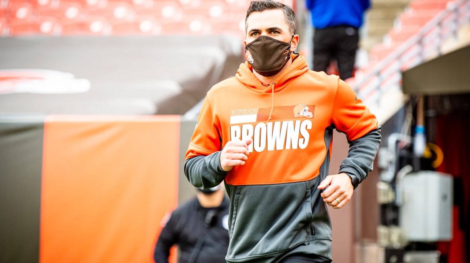 Kevin Stefanski runs onto the field in his Browns hoodie wearing a facemask.