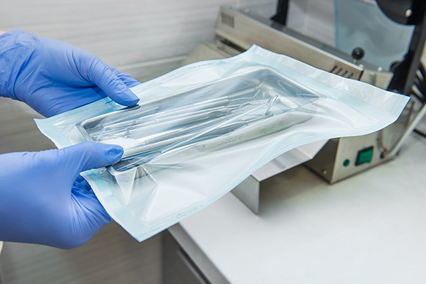 Gloved hand of a medical professional holding a vacuum-sealed packet of sterilized medical equipment.