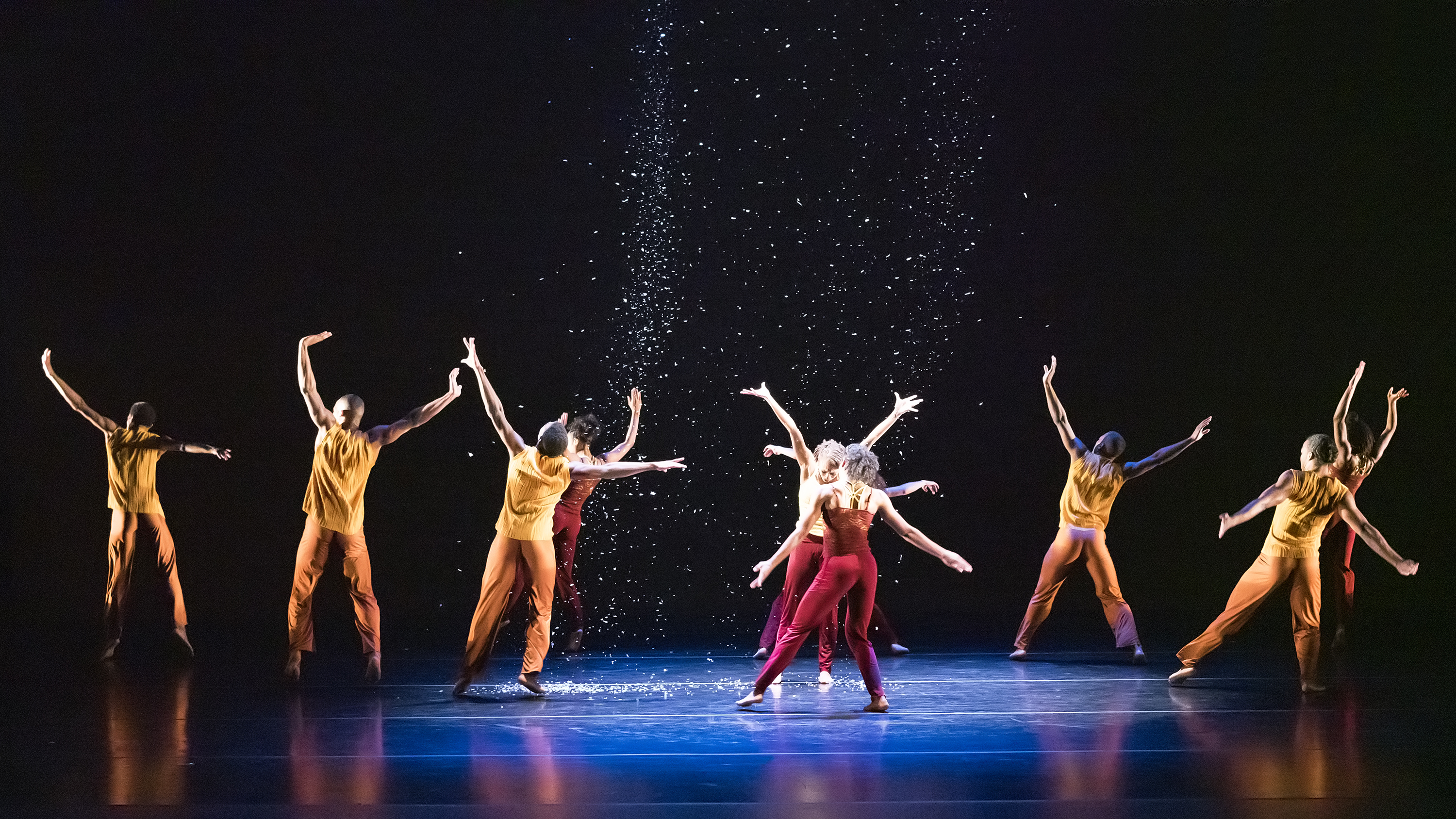 Modern dancers with arms outstretched perform in a spotlight as confetti rains 