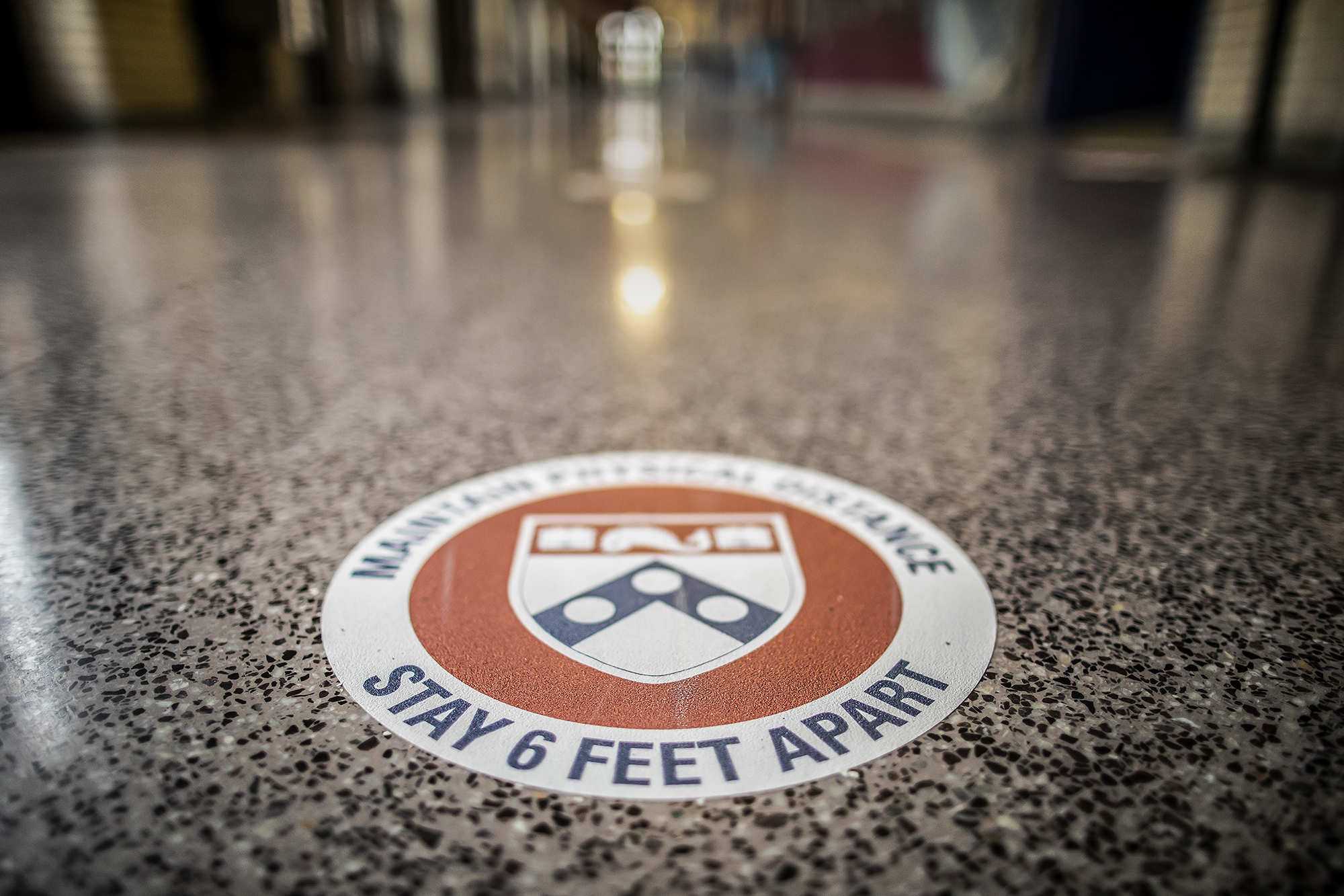 A round decal on the floor that reads MAINTAIN SOCIAL DISTANCE STAY SIX FEET APART surrounding the Penn shield logo.