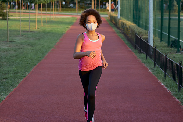 Young person running laps on a track wearing a face mask.