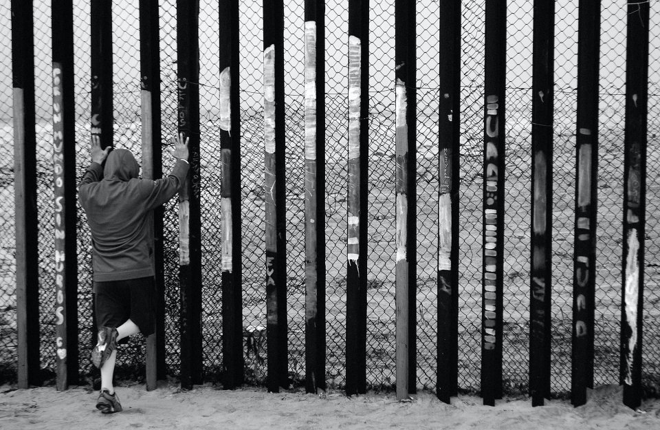 Young person pressing hands up against a border wall.