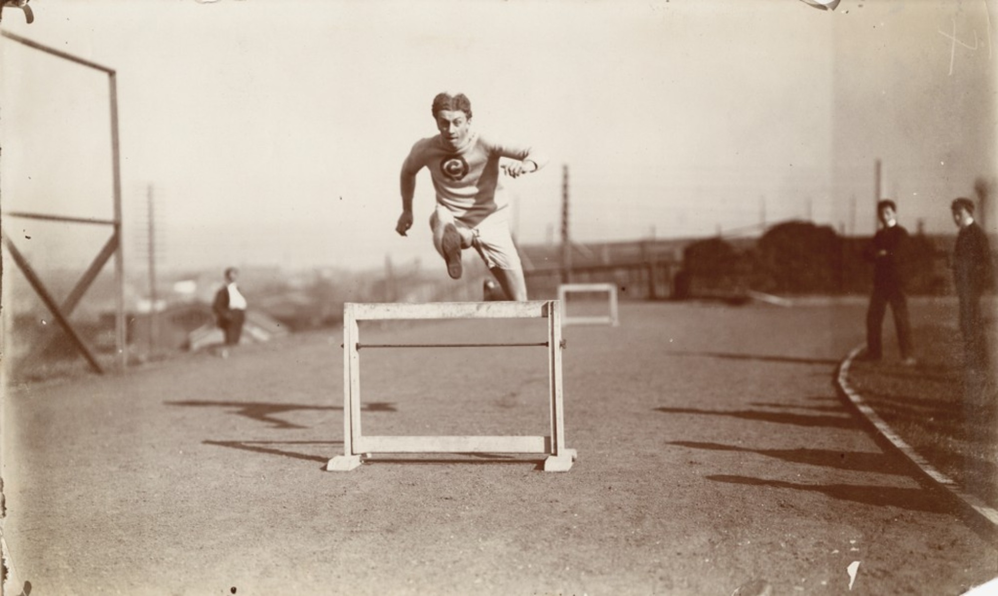 Alvin Christian Kraenzlein jumps over a hurdle while wearing a sweat suit circa 1900.