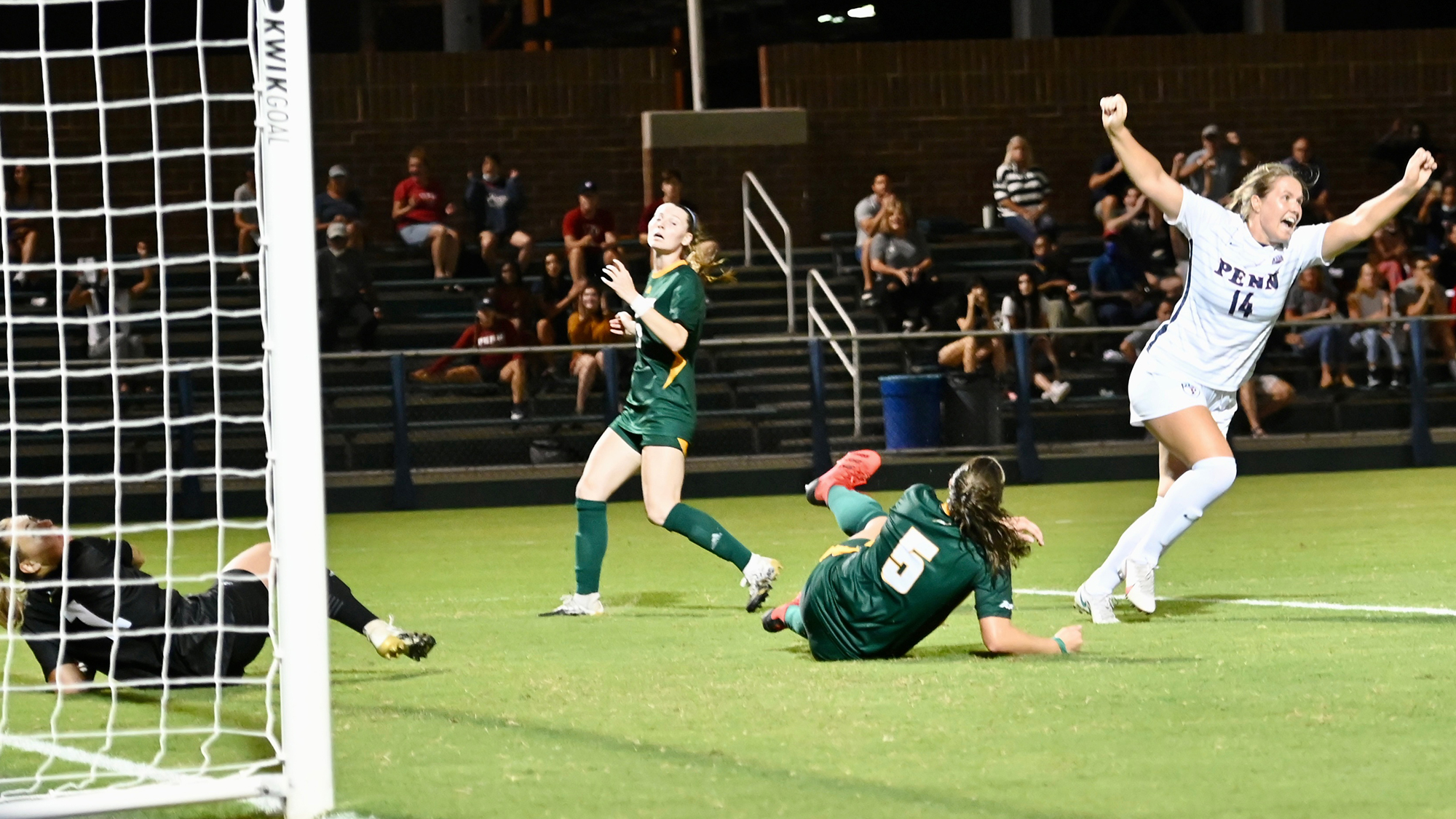 Shenk celebrates with her arms raised after scoring a goal.