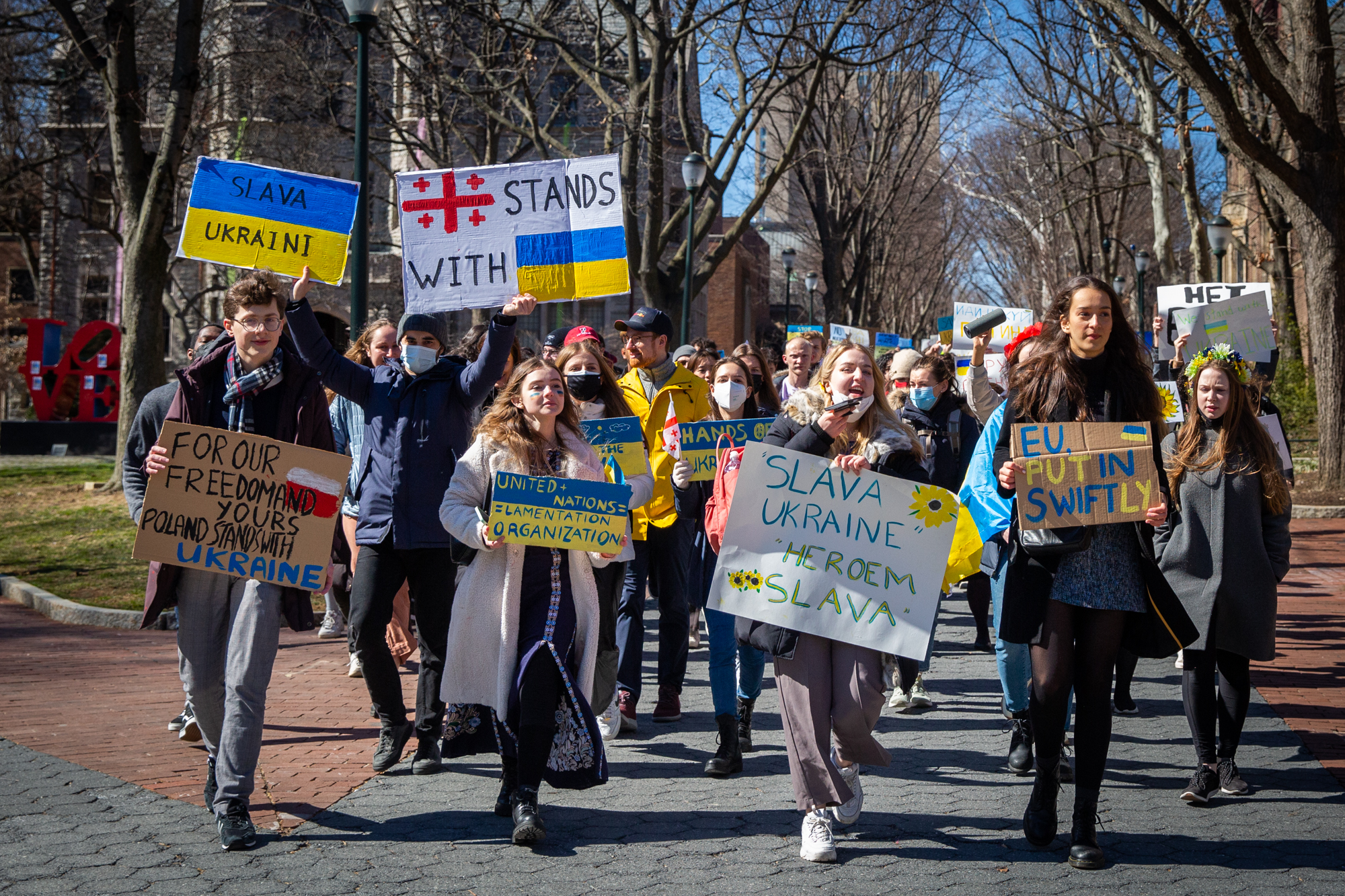 A group of students holding Ukrainian solidarity signs walk down Locust Walk.