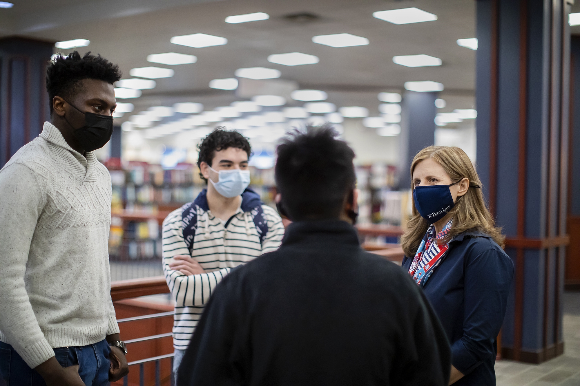 Liz Magill stands in the Penn Bookstore talking with three masked people from Penn.