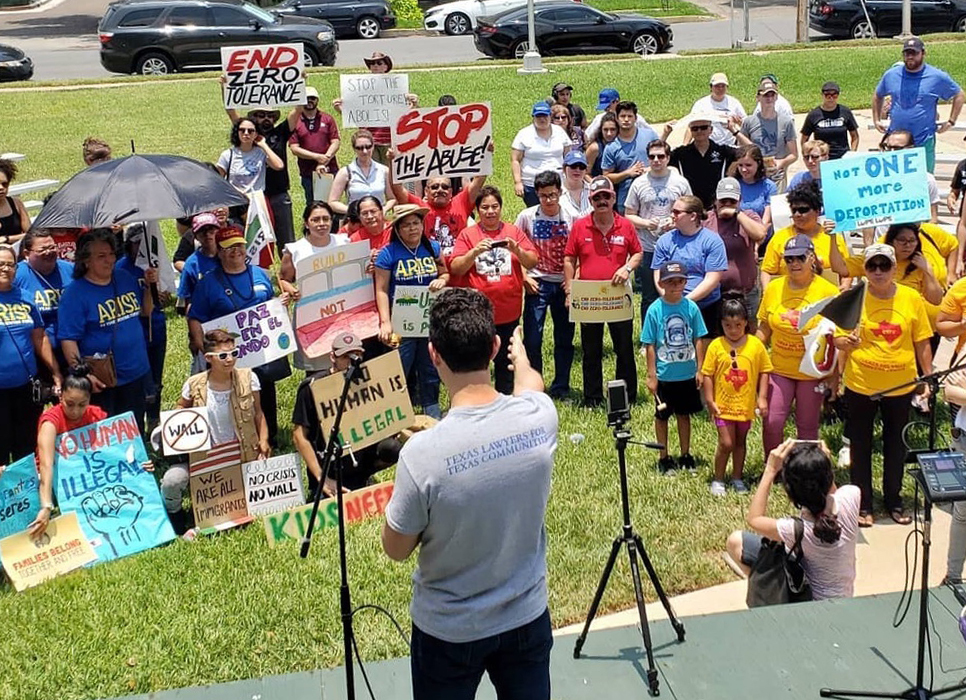 Efrén Olivares speaks to a crowd of people holding signs that say "end zero tolerance," "no human is illegal," and "not one more deportation."