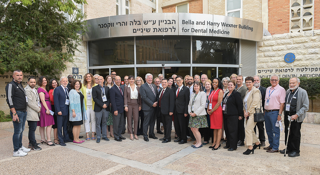 Roughly two dozen people stand in front of the Bella and Harry Wexner Building for Dental Medicine in Israel