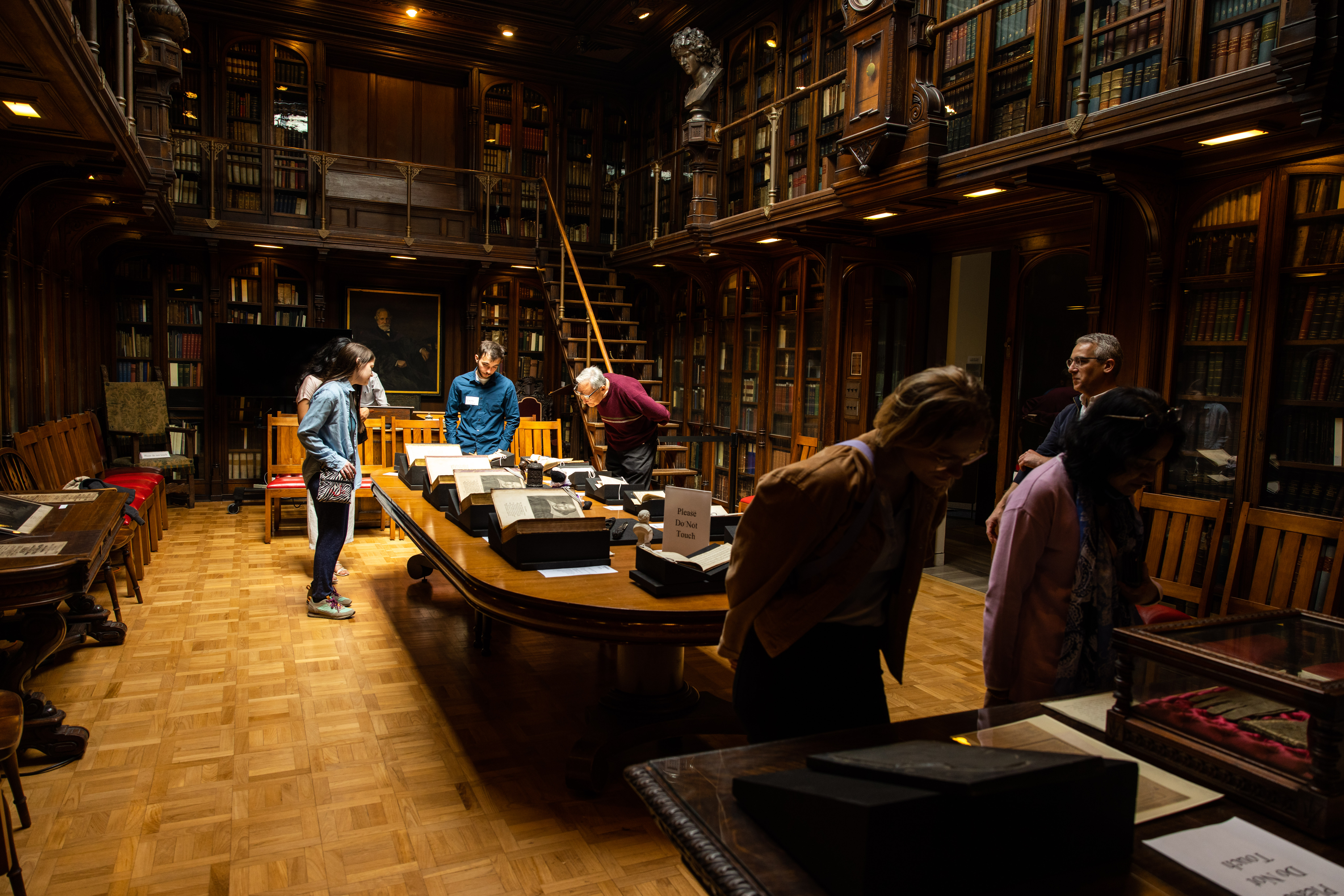 about six people in a historic library looking at books on a long table