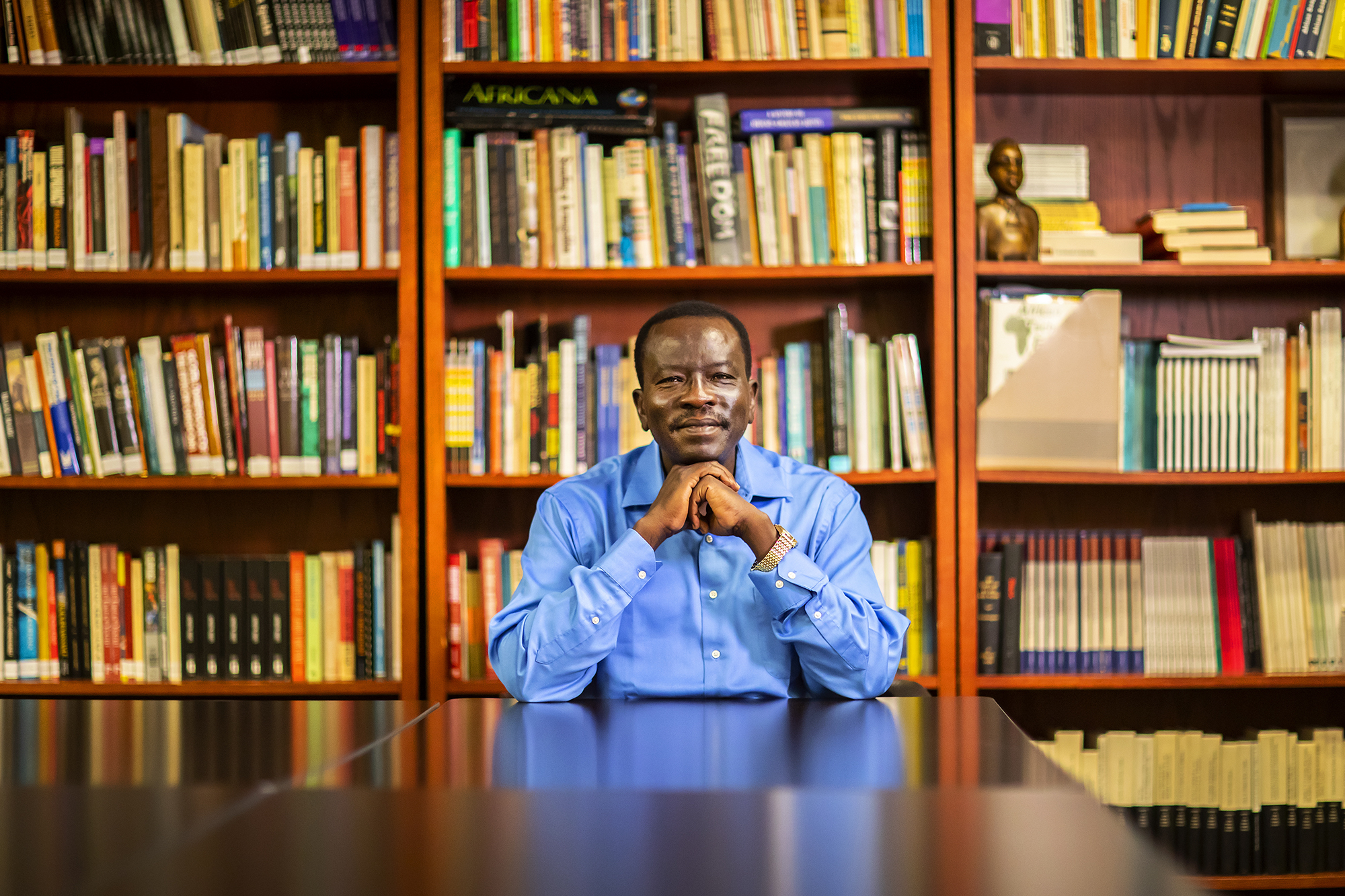 Sudanese scholar and Penn lecturer Ali Ali-Dinar sits at table with his elbows on the table, clasping his fists under his chin, in front of a large bookcase.