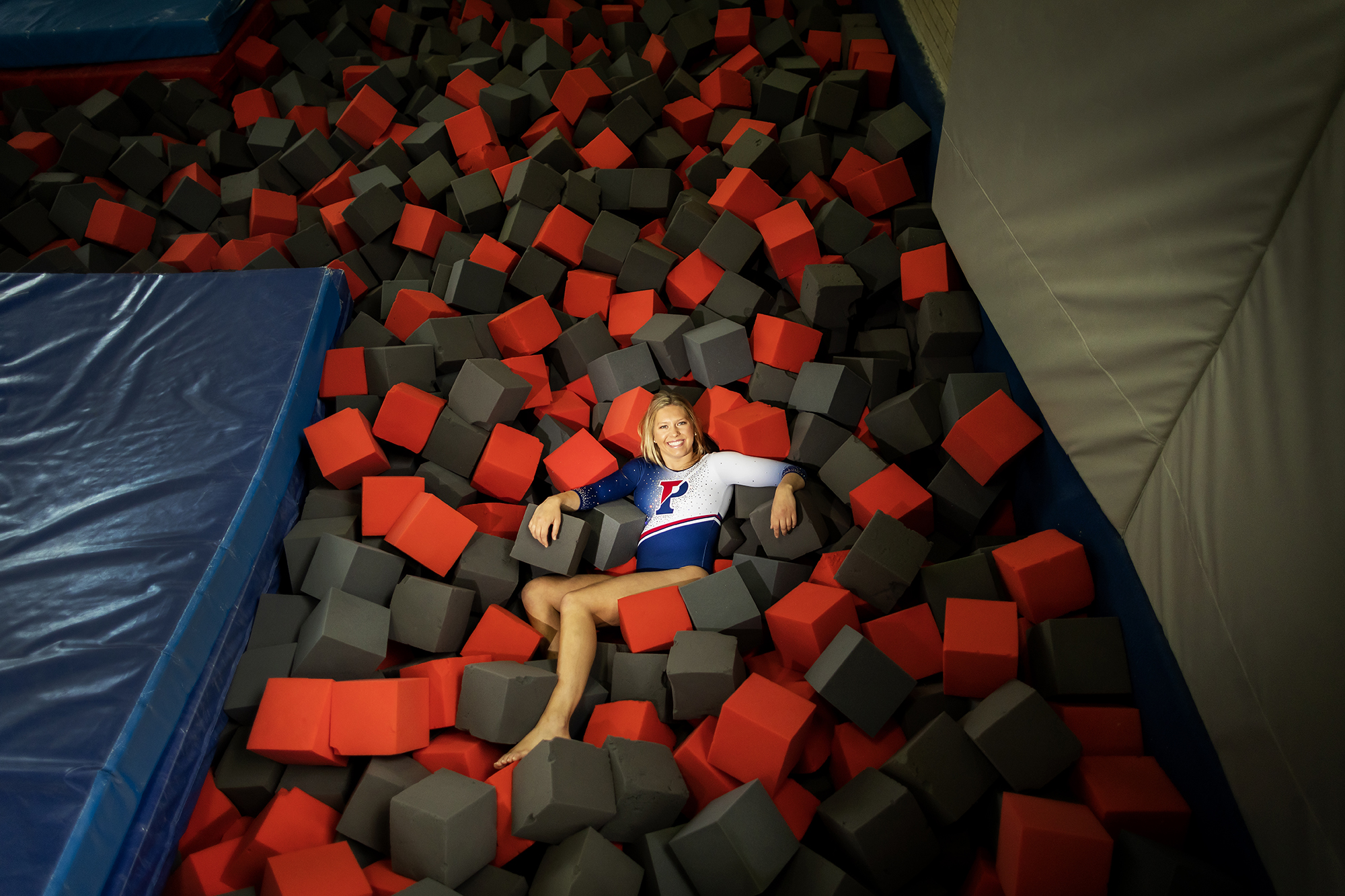McCaleigh Marr, wearing her Penn leotard, lies in a pile of foam squares, next to a mat.