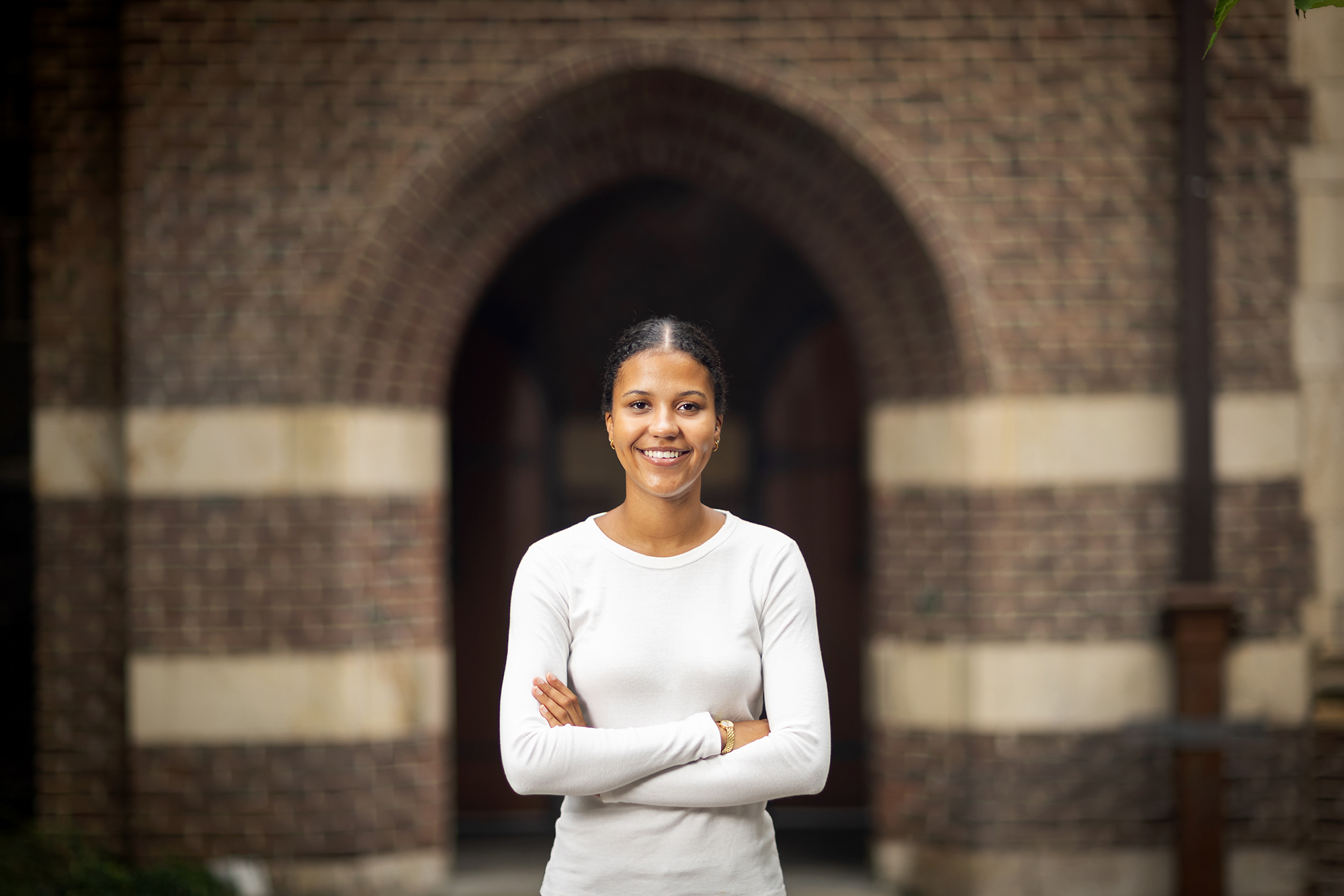 Penn rising fourth-year Sophie Mwaisela stands in front of a brick archway with her arms crossed.