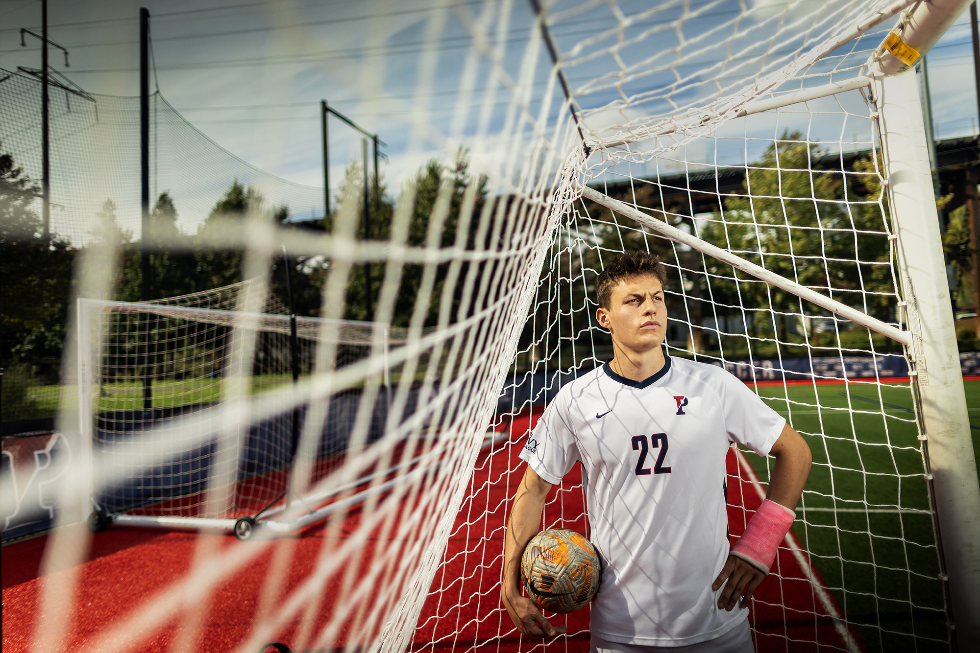 Stas Korzeniowski stands inside a goal at Penn Park holding a soccer ball on his right side.