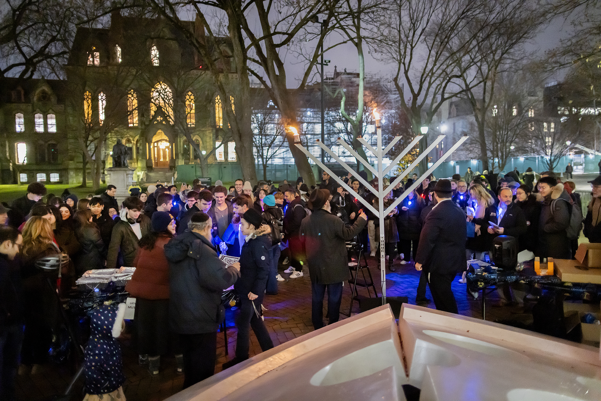 A crowd of people by a large menorah in front of College Hall.