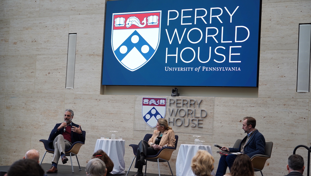 Three people sit on a stage in front of a screen reading Perry World House, University of Pennsylvania.