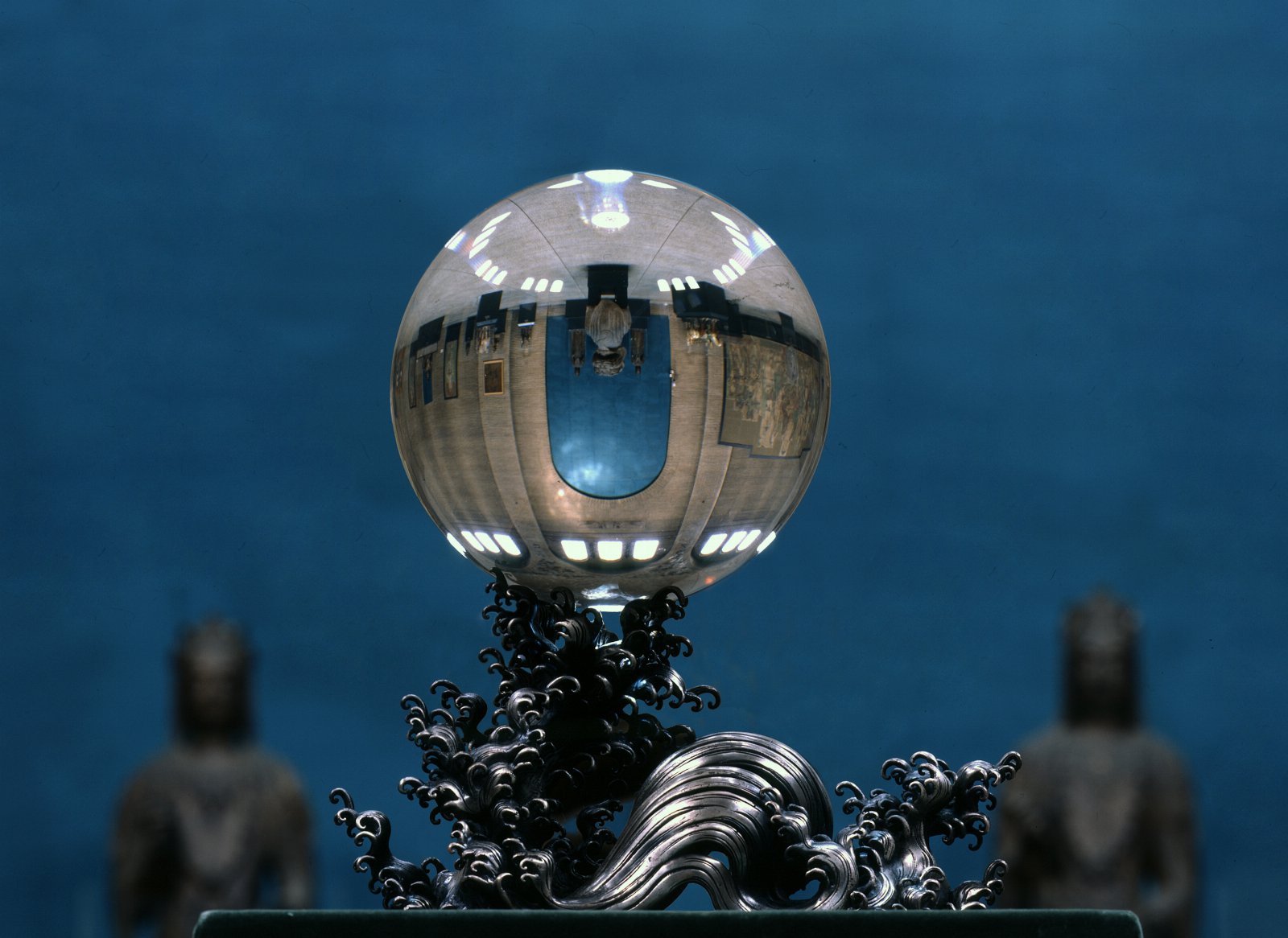 An image of the crystal ball on its silver stand flanked by two statutes in the Asia Galleries
