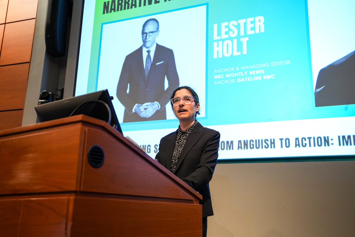 Penn Carey Law Dean Sophia Lee speaks at a podium with a screen featuring an image of NBC's Lester Holt behind her.